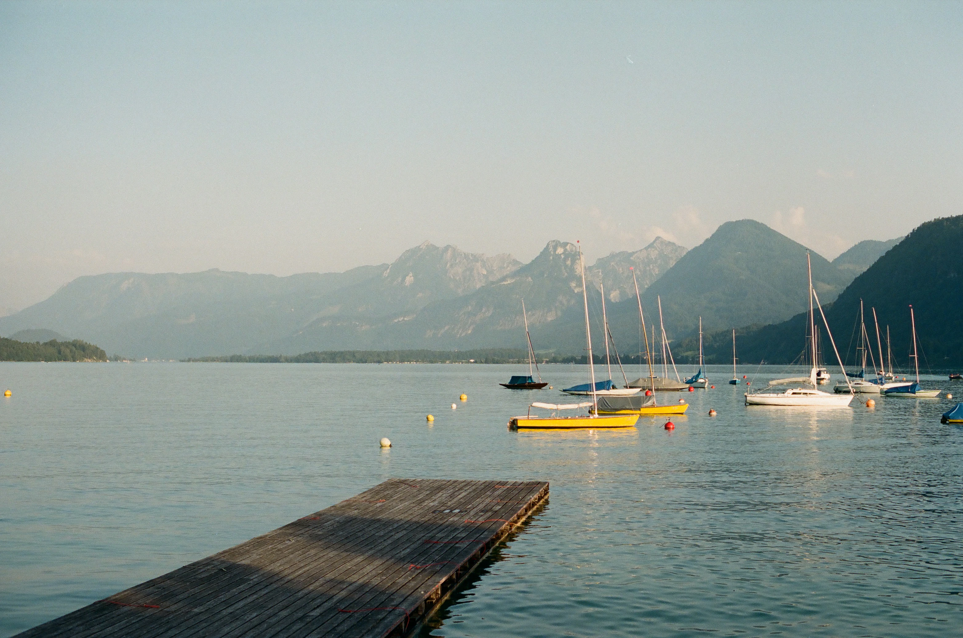 Sailboats moored on a calm lake with mountains in background.