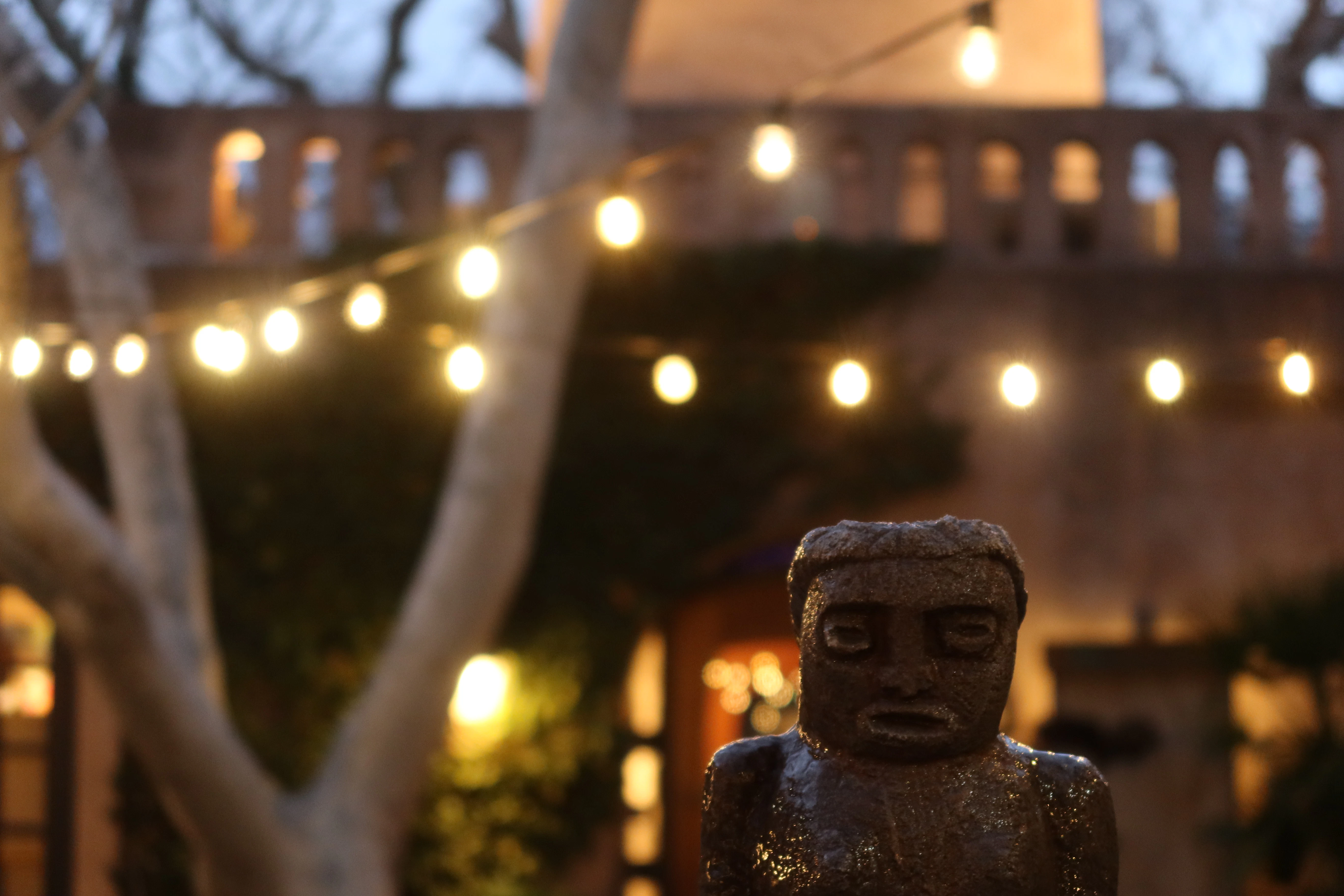 String lights illuminate a courtyard with a statue.