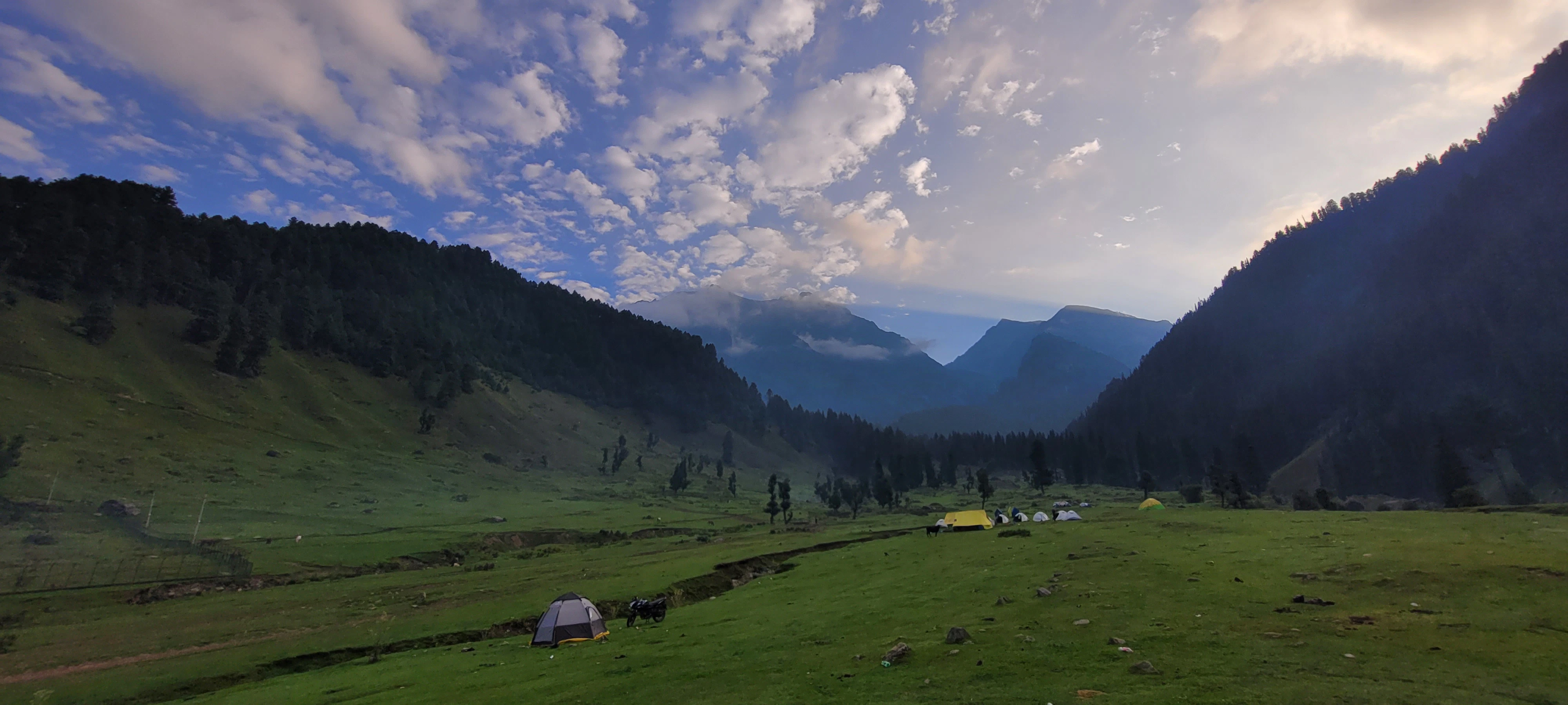 a grassy valley with tents and mountains in the background