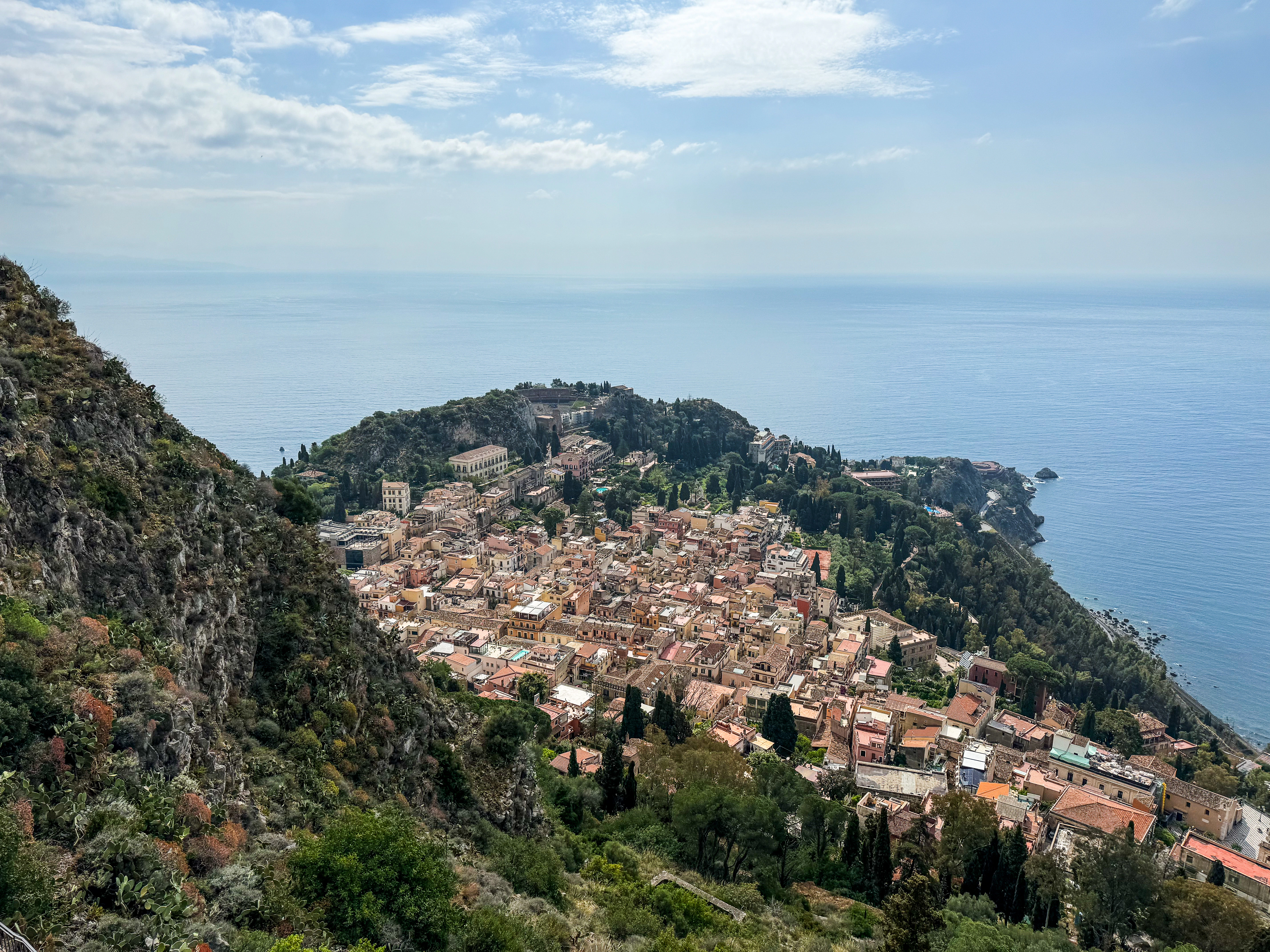 Hillside town overlooking the blue ocean under a cloudy sky.