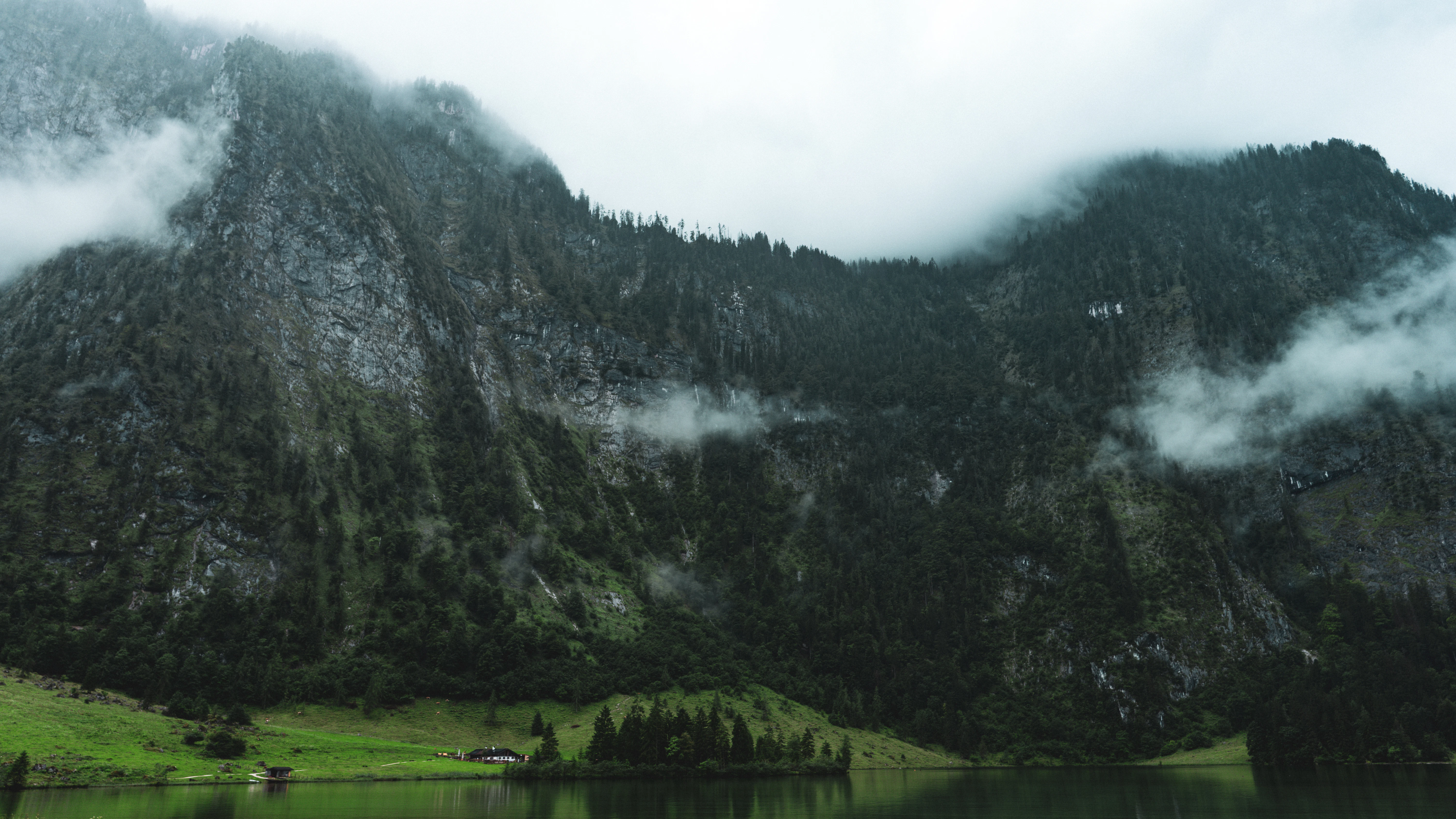 Mountains and trees are covered in fog over water.