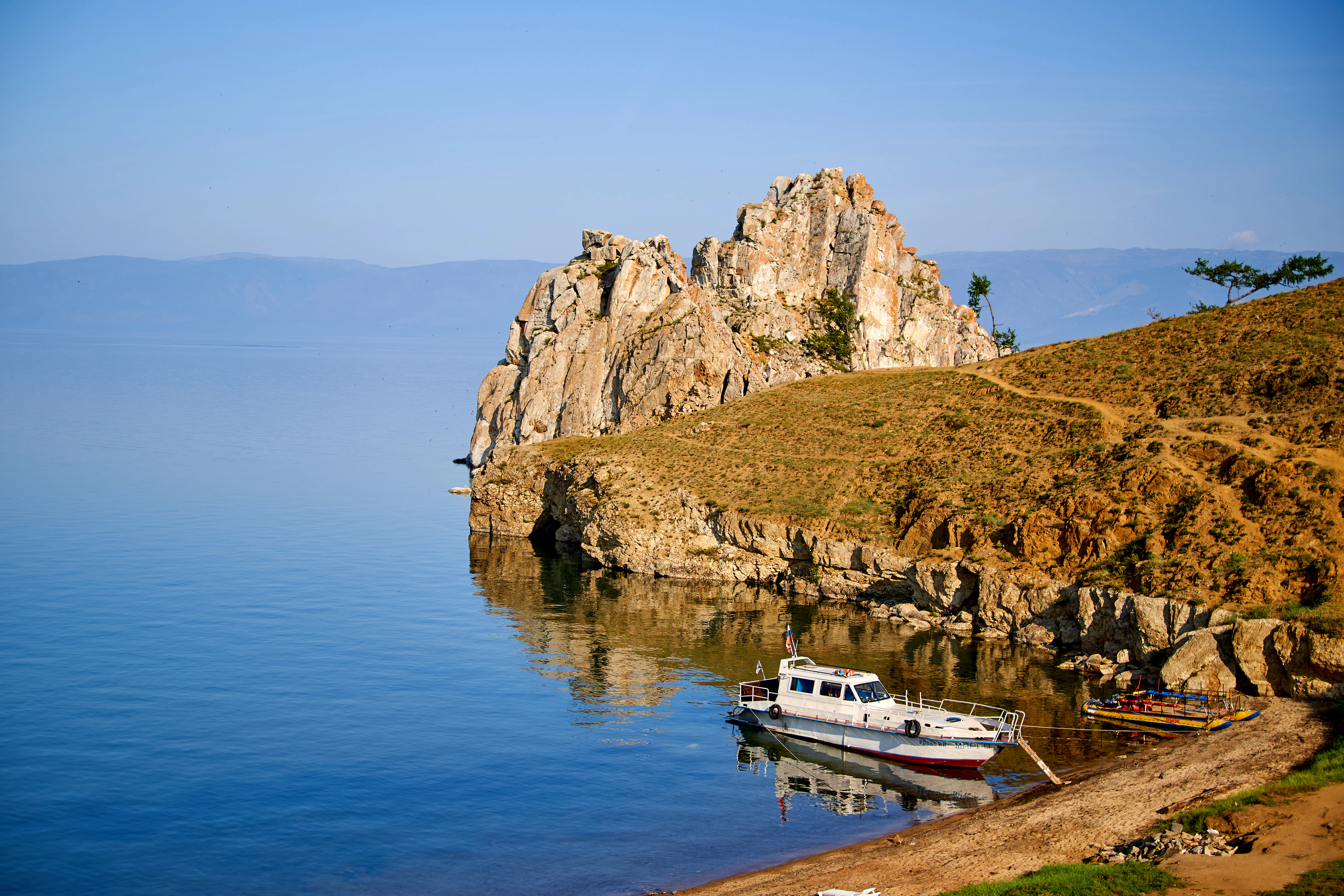 white boat on body of water near brown and green mountain during daytime